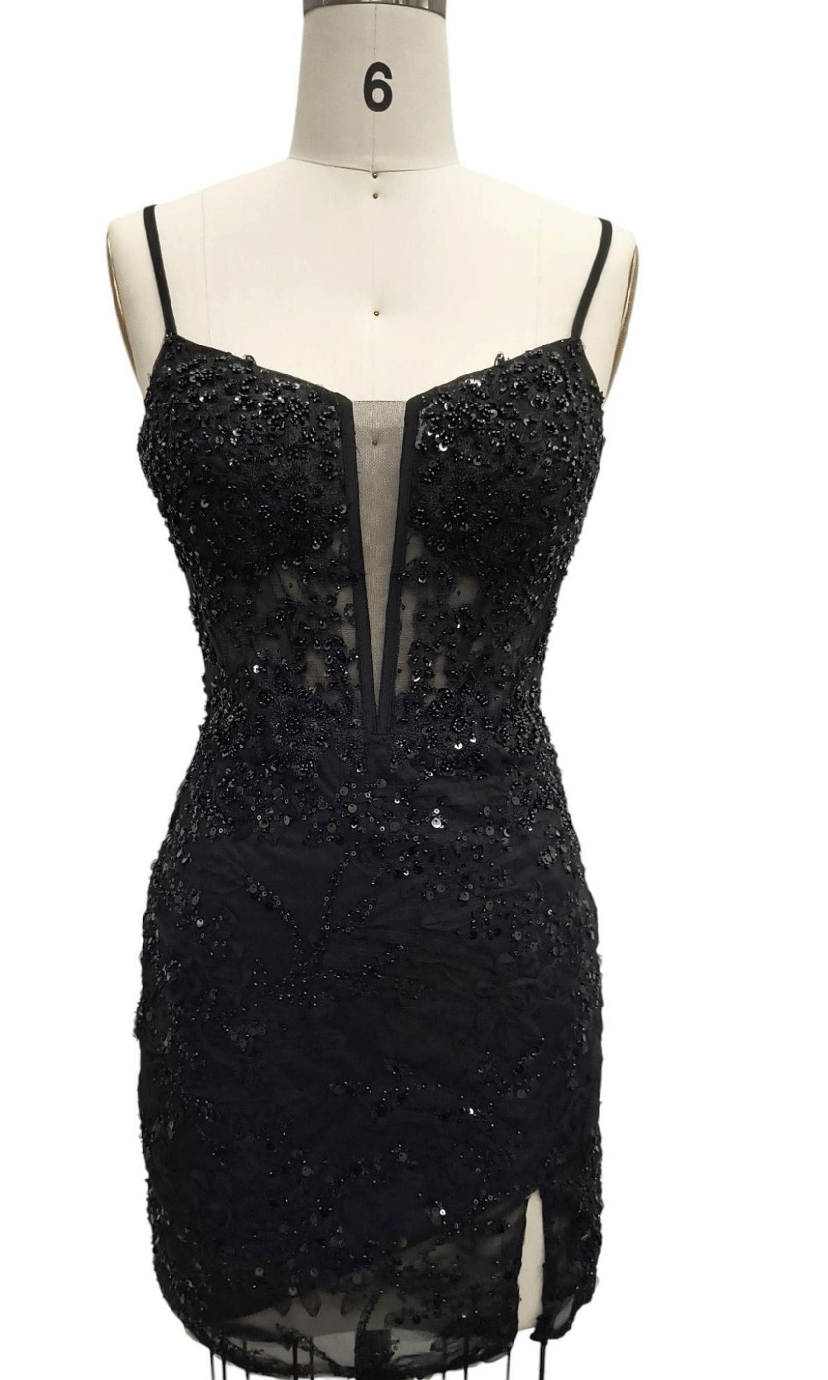 The Short Black Sequin Hoco Dress: 12660 features thin straps, a sheer mesh neckline panel, decorative beading, and a fitted silhouette. Displayed on a dress form.